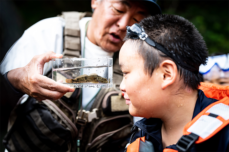 ジオキャンプin上野村 自然体験イベントで、子どもが水槽の生き物を観察している様子